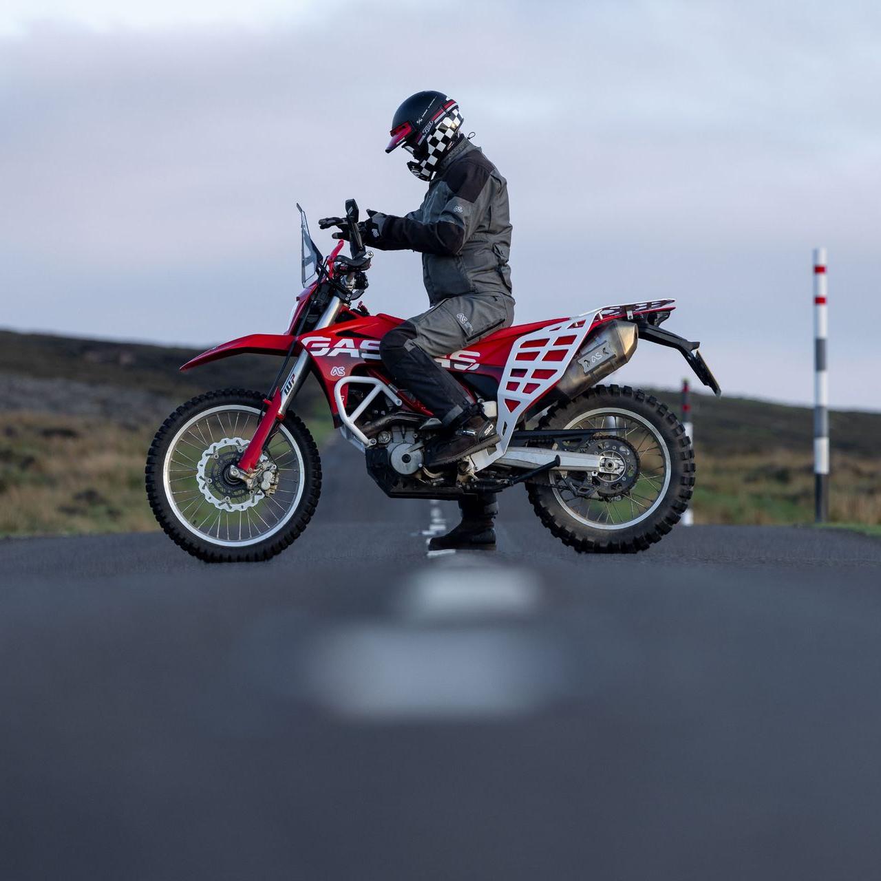 rider sitting on red gasgas es700 motorcycle on road during dusk adjusting gloves